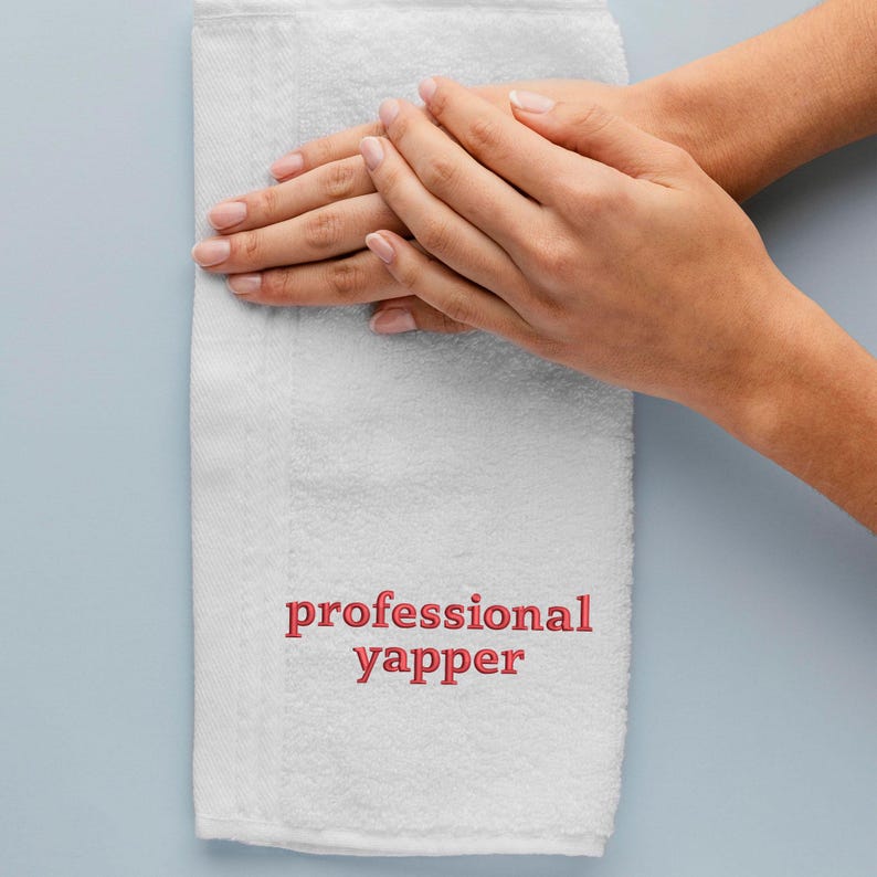 May include: White hand towel with the words "professional yapper" embroidered in red.