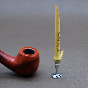 May include: A wooden pipe with a red finish and a metal pipe tool with a yellow handle. The tool has the words "Slow Puff, Long Life" engraved on it.
