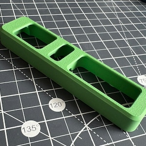 May include: A green plastic tool with three rectangular slots. The tool is designed to help with woodworking projects.