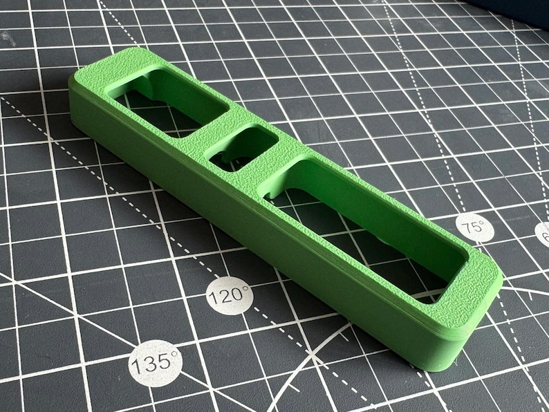May include: A green plastic tool with three rectangular slots. The tool is designed to help with woodworking projects.