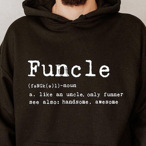 May include: Black hooded sweatshirt with the word "Funcle" printed in white. The definition of "Funcle" is also printed below the word. The sweatshirt has a front pocket and a drawstring hood.