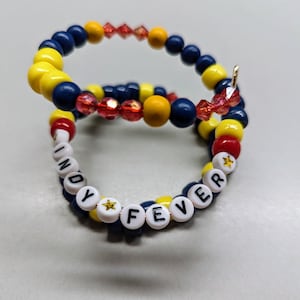May include: Two beaded bracelets, one with blue, yellow, and red beads, and the other with white beads spelling out "INDY FEVER" with gold stars.