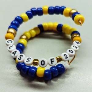 May include: A blue and yellow beaded bracelet with white beads spelling out "CLASS OF 2024".