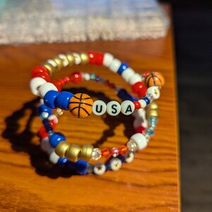 May include: Three beaded bracelets with red, white, and blue beads, along with basketball charms and the letters "USA".