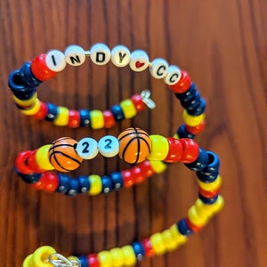 May include: Three beaded bracelets with a basketball theme. The top bracelet has the letters "INDY" with a heart and "C" beads. The middle bracelet has two basketball beads and the numbers "22". The bottom bracelet has a silver charm.