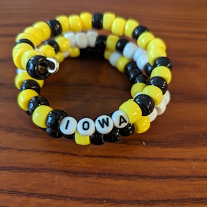 May include: A yellow, black, and white beaded bracelet with the word "IOWA" spelled out in white beads.