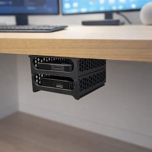 Könnte beinhalten: Schwarze Computerhalterung für unter dem Schreibtisch mit zwei übereinander angeordneten Fächern. Die Halterung besteht aus Kunststoff mit Wabenmuster und ist für kleine elektronische Geräte konzipiert. Die Halterung ist an der Unterseite eines hellen Holzschreibtisches befestigt.