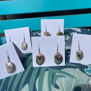 May include: Five pairs of iridescent abalone shell earrings on white display cards. The earrings are silver tone and feature a variety of abalone shell colors and patterns.