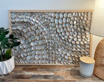 Può includere: Un'opera d'arte da parete incorniciata realizzata con conchiglie di abalone iridescenti disposte in un motivo a spirale. Le conchiglie sono incastonate in una cornice in legno chiaro.