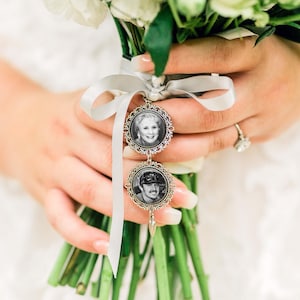 May include: A white bridal bouquet with a silver charm attached. The charm has two round photo frames with black and white photos of a man and a woman.