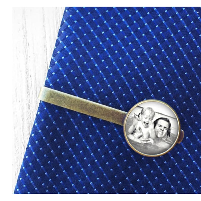 May include: A gold tie bar with a round, black and white photo of a father and child in a pool. The photo is set in a silver frame.