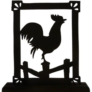 May include: Black silhouette of a rooster standing on a fence post, framed in a black square with decorative flourishes. The rooster is facing right and has its head tilted up. The silhouette is mounted on a black base.
