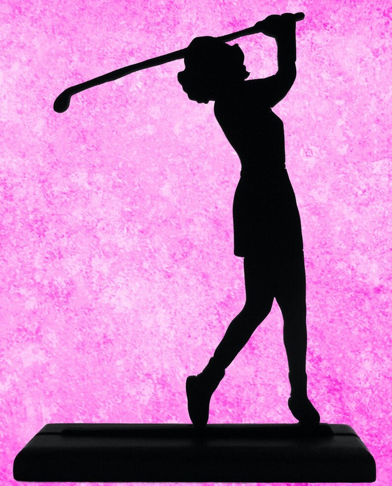 Puede incluir: Silueta negra de una golfista en pleno swing, sosteniendo un palo de golf. La figura se encuentra sobre un fondo rosa texturizado. La golfista est&aacute; sobre una base rectangular negra.
