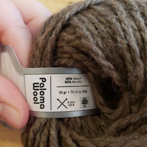 May include: A ball of brown Paloma Wool yarn. The label indicates it is 40% wool and 60% acrylic, with 75 m of yarn per 50 gr. The label also indicates the yarn is 5 mm and US size 8.