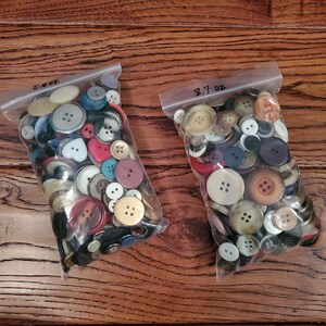 May include: Two clear plastic bags filled with a variety of colorful buttons. The bags are labeled "8.7 oz" and "7.0 oz".