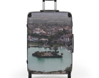 Puede incluir: Maleta negra con una imagen impresa de una ciudad y un lago. La ciudad está rodeada de árboles y el lago es de color azul claro.