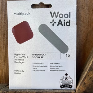 May include: A multipack of 15 Wool + Aid Hyperfine Merino Wool Adhesive Bandages, 10 regular 5 square bandages. The packaging is white with red and gray accents. The packaging features the text "Wool + Aid" and "Hyperfine Merino Wool Adhesive Bandages". The packaging also features the text "10 Regular 5 Square" and "15". The packaging also features the text "Naturally Better". The packaging also features the text "Performance" and "Sustainable". The packaging also features the text "Naturally Breathable, Sterile, Flexisoft Comfort" and "Plastic Free Fabric, Merino Wool, Renewable Wool Fibre". The packaging also features the text "Outdoor Retailer Innovation Awards Winner".