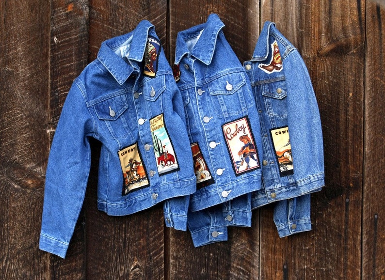 May include: Three blue denim jackets with various cowboy-themed patches. The patches feature cowboys, horses, cacti, and the word "Cowboy".