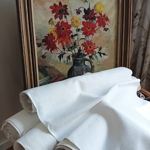 Könnte beinhalten: Ein gerahmtes Gemälde mit einem Strauß roter und gelber Blumen in einer Vase. Das Gemälde lehnt an einem Stapel weißer Stoffrollen.