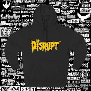 Könnte beinhalten: Schwarzer Kapuzenpullover mit gelbem, verwittertem "DISRUPT"-Schriftzug auf der Brust. Der Hoodie hat eine Kapuze mit Kordelzug und eine Kängurutasche. Der Hintergrund ist mit verschiedenen Bandlogos und Texten gefüllt.