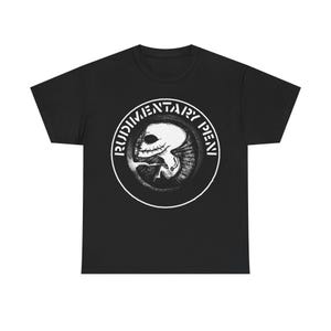 Könnte beinhalten: Schwarzes T-Shirt mit einem kreisförmigen Grafikdesign. Der Text "RUDIMENTARY PENI" umrandet den Rand. Die zentrale Grafik ist ein detaillierter, stilisierter Schädel mit einem dunklen, schattigen Design. Das T-Shirt ist aus weichem Material.