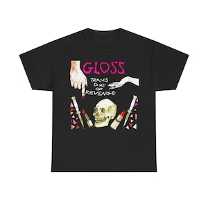 Puede incluir: Camiseta negra con un diseño gráfico que presenta la palabra "GLOSS" en rosa, una calavera, lápiz labial y cuchillos. El texto "TRANS DAY OF REVENGE" también está incluido en el diseño.