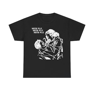 以下が含まれることがあります： 2 人の人物が抱き合っている白いグラフィックイラストが特徴の黒いTシャツ。触手のある生き物が描かれています。「METH WAX」の文字がイラストの上に3回印刷されています。