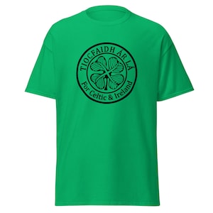 May include: A vibrant green t-shirt with a black circular design. The design includes a four-leaf clover and the text "TIOCFAIDH ÁR LÁ" above "For Celtic & Ireland". The shirt is made of a soft material and has short sleeves.