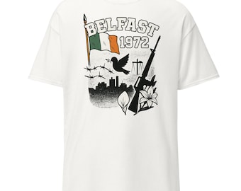 May include: White t-shirt featuring a graphic design with the text "Belfast 1972". The design includes the Irish flag, a dove, a rifle, barbed wire, and a cityscape silhouette. The shirt is made of a soft material.