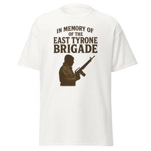 Puede incluir: Camiseta blanca con un gráfico y texto marrón. El gráfico muestra la silueta de una persona sosteniendo un rifle. El texto dice "IN MEMORY OF THE EAST TYRONE BRIGADE."