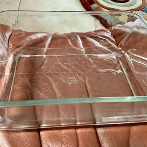 May include: A clear, rectangular glass baking dish. The dish has straight sides and a flat bottom. The words "MADE IN USA" are visible on the glass. The dish is empty and appears to be unused.