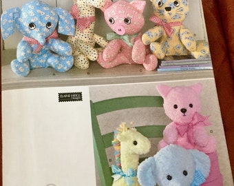 May include: Simplicity sewing pattern featuring stuffed animal designs. The pattern includes instructions for making a blue elephant, giraffe, pig, cat, and bear. The animals are made of patterned fabric and have ribbon accents.