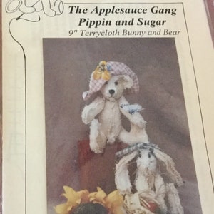 May include: A printed image featuring two terrycloth dolls: a bear and a bunny. The bear, wearing a hat, is above the bunny, which holds a basket. The text reads "Beardeaux Bears" and "The Applesauce Gang Pippin and Sugar 9" Terrycloth Bunny and Bear."