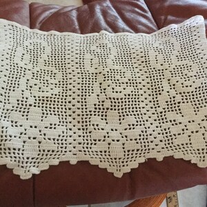 May include: Cream-colored, hand-crocheted doily with a scalloped edge. The intricate openwork design features repeating floral and geometric patterns. This vintage textile is likely used as a decorative table covering or accent piece.