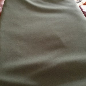 May include: Close-up of a folded piece of olive green fabric. The fabric has a subtle ribbed texture and appears to be a medium-weight material. The color is a muted, earthy tone, suggesting a natural fiber textile.