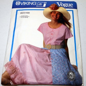May include: Vogue Patterns sewing pattern packet. The packet features a woman wearing a pink dress with a blue floral skirt. The dress has a round neckline and short sleeves. The woman is wearing a straw hat with a flower and a woven belt.