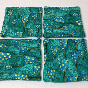 Puede incluir: Cuatro posavasos cuadrados de tela con un fondo verde azulado y un patr&oacute;n repetido de flores estilizadas azules y amarillas. Los posavasos est&aacute;n hechos de una tela suave y texturizada.