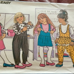 May include: Vintage sewing pattern featuring illustrations of four young girls in various outfits. The girls are wearing jumpers, dresses, and overalls. The text "FAST & EASY" is at the top, with "EASY FUNWEAR" below. The pattern number is 5130.