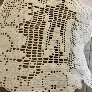 May include: A white, handmade crochet doily with a floral design. The intricate openwork pattern creates a delicate and airy texture. The doily is likely used as a decorative piece for tables or other surfaces.