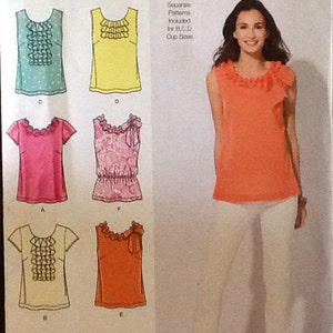 May include: Simplicity sewing pattern 2599 featuring various blouse designs with ruffle and bow details. The pattern includes sizes 12-20 and is suitable for B, C, and D cup sizes. The image shows a woman wearing an orange blouse and white pants.