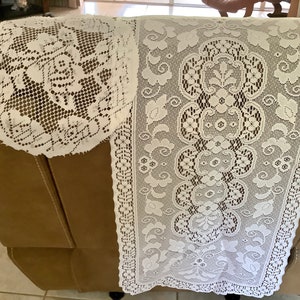 May include: White lace doily and runner set. The doily is round with a floral pattern, and the runner features a repeating floral design with a scalloped edge. The lace is delicate and adds a vintage touch.