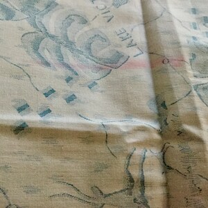 May include: Cream-colored fabric with a map-like design featuring blue and pink accents. The fabric has a textured appearance, with visible details of a map including the words "KENYA" and "LAKE VICTORIA".