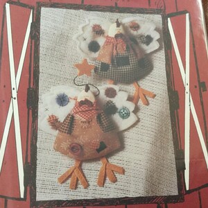 May include: Two handmade turkey ornaments with felt wings, plaid bodies, and orange felt feet. Each turkey has a red and white checkered scarf and button accents. One has a star, the other has a button.