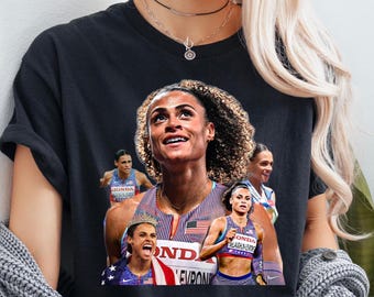 May include: Black t-shirt featuring a collage of images of an athlete. The images include the athlete in various poses, wearing athletic gear with the American flag and the word "HONDA" visible. The athlete is smiling and looking upwards.