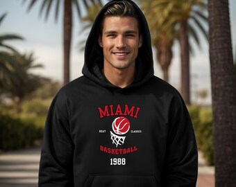 Może przedstawiać: Czarna bluza z kapturem z napisem "MIAMI BASKETBALL 1988" w kolorze czerwono-białym. Projekt zawiera koszykówkę i siatkę. Bluza ma przednią kieszeń i kaptur.