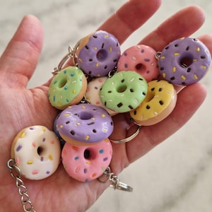 May include: A collection of colourful donut-shaped keyrings with different sprinkles and frosting. The keyrings are made of polymer clay and are attached to silver key rings.