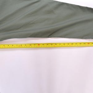 May include: An olive green garment sleeve with a yellow measuring tape laid across it. The tape measure shows a length of approximately 76 cm. The sleeve has a velcro patch at the cuff.