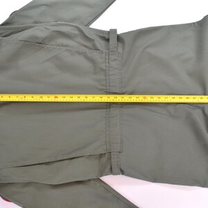 May include: Olive green jumpsuit with a yellow measuring tape laid across the front. The jumpsuit has a collar, pockets, and a belt loop. The measuring tape shows a length of approximately 76 cm.