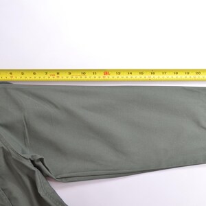 May include: A close-up of a sage green jacket sleeve with a yellow measuring tape laid across it. The sleeve has a velcro closure at the cuff. The measuring tape shows a length of approximately 61 cm.