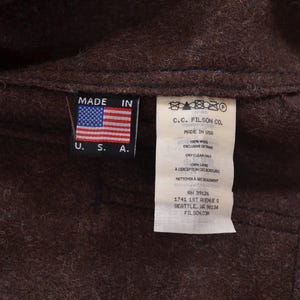May include: Close-up of a brown wool garment with two tags. One tag displays the American flag and reads "MADE IN U.S.A.". The other tag has text including "C.C. FILSON CO." and care instructions.